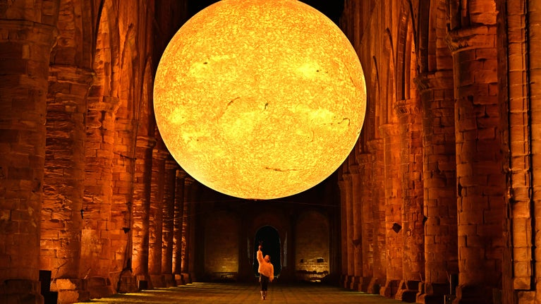 A child stands underneath a huge sun artwork in Fountains Abbey